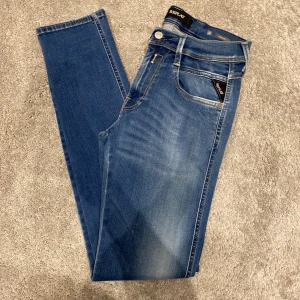Replay anbass jeans - Snygga blå jeans från Replay med klassisk femficksdesign och diskreta slitningar framtill. Jeansen har smal passform och normal midja, med detaljerade sömmar på bakfickorna. Perfekta för dig som gillar en stilren och modern look.