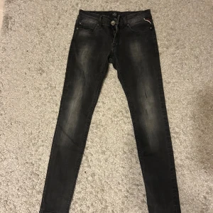 Replay jeans  - Svarta skinny jeans från Replay med diskret slitning och klassisk femficksdesign. Byxorna har en smal passform, normal midja och detaljerad bakficka med röd Replay-logga. Perfekta för dig som gillar en stilren och modern look.