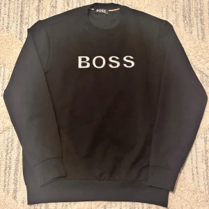 Svart sweatshirt från BOSS - Svart sweatshirt från BOSS med broderad logga i vitt framtill. Klassisk rund halsringning och långa ärmar. Mjuk och skön bomullsblandning som passar perfekt till jeans eller joggers.