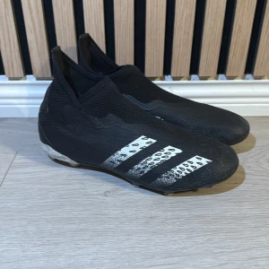 Svarta adidas fotbollsskor med taggar - Säljer ett par svarta adidas fotbollsskor med vita ränder och coolt leopardmönster på ovansidan. Skorna har en strumpliknande passform utan snörning och är tillverkade i syntetmaterial för bästa grepp och komfort på planen. Sulan har dobbar för extra fäste.