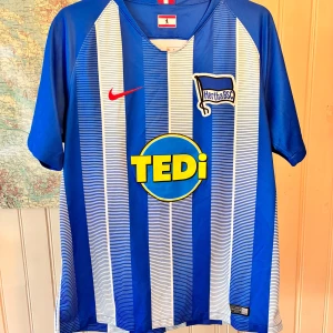 Hertha BSC Nike 2018/19 home shirt, size L - Barely used  #herthabsc #bundesliga #nike #selke #kalou #ibisevic #vintage  Blåvitrandig fotbollströja med Hertha BSC-märke och sponsorlogotypen ”Tedi” på framsidan. Tröjan har en röd Nike-logga på bröstet och en liten Berlin-flagga under kragen. På baksidan finns en röd och vit detalj vid nacken och en Hyundai-logotyp på ärmen.