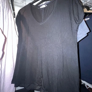 Svart t-shirt med v-ringning - En enkel svart t-shirt med v-ringad hals och korta ärmar. Modellen är klassisk och har en loose passform som gör den skön att bära. Materialet känns mjukt och lätt, perfekt för dig som gillar stilrena basplagg.