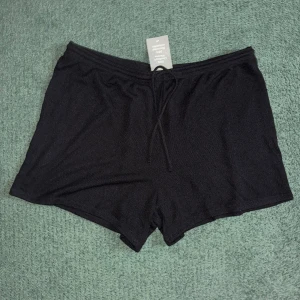 Svarta shorts med snörning från H&M - Svarta shorts från H&M i storlek XL, tillverkade i en mjuk och stickad blandning av 50% LivaEco viskos och 50% återvunnen polyester. De har elastisk midja med snörning och en loose passform, perfekta för chill dagar eller sommarhäng.