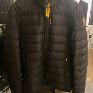 Svart dunjacka från Parajumpers - Svart dunjacka från Parajumpers med broderad patch på ärmen och cool gul detalj vid halsen. Jackan är quiltad och har dragkedja framtill samt fickor med dragkedja. Superlätt material som gör den smidig att bära. Perfekt för kalla dagar.