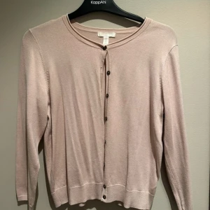 Beige kofta  - Snygg beige kofta från HM med rund halsringning och svarta knappar framtill. Långärmad och i mjukt, tunt material. 