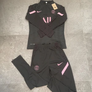 Psg x Nike tracksuit  - Säljer en svart långärmad PSG tracksuit från Nike med rosa detaljer.Tröjan har halv dragkedja, broderat PSG-märke och Nike logga. För bästa komfort vid träning. Snygg och modern design. Dunder kvalité på den✨