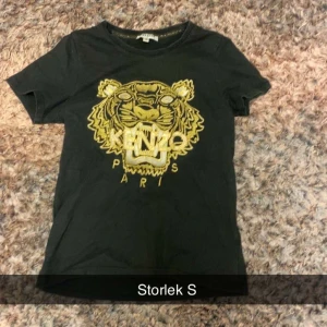 Svart Kenzo t-shirt med tigertryck - Svart t-shirt från Kenzo i storlek S med ikoniskt gult tigertryck och broderad logga på bröstet. Klassisk rund hals och korta ärmar. Perfekt för dig som gillar statement-plagg och streetstyle.