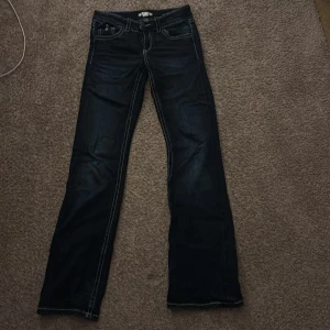 Mörkblå bootcut jeans Gina Tricot - Snygga mörkblå jeans från Gina Tricot i storlek 158. Modellen har bootcut-ben och kontrastfärgade sömmar. Klassisk femficksdesign med knappar på bakfickorna och dragkedja fram. Perfekta för dig som gillar retrovibbar och markerade detaljer.