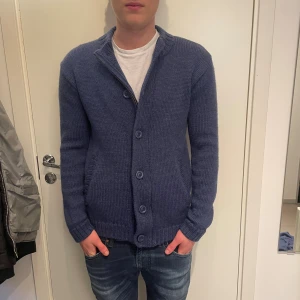 Stickad cardigan  - Mysig blå stickad kofta med både knappar och dragkedja framtill. Koftan har ribbade muddar, två fickor och en klassisk krage. storlek S men passar M.