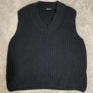 Svart stickad väst från Gina Tricot - Svart stickad väst från Gina Tricot i storlek S. Västen har en ribbad struktur och v-ringad hals, vilket ger en snygg och modern look. Perfekt att styla över en skjorta eller t-shirt för en trendig vibe.