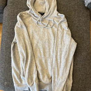 Ljusgrå hoodie från H&M Relaxed Fit - Ljusgrå hoodie från H&M i relaxed fit med huva och snörning. Tröjan har en klassisk känguruficka framtill och är tillverkad i mjuk bomullsmix. Perfekt för chill dagar och enkel att matcha med jeans eller joggers.
