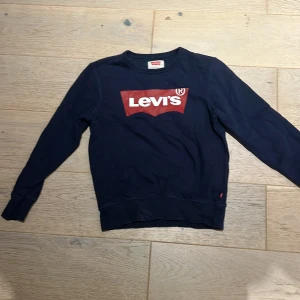 Mörkblå Levi's sweatshirt med logga - Mörkblå sweatshirt från Levi's med klassisk röd och vit logga framtill. Tröjan har rund halsringning, långa ärmar och ribbade muddar. Perfekt för dig som gillar streetstyle och vill ha en enkel men snygg look.
