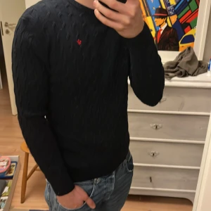 Svart kabelstickad tröja från Morris - Svart kabelstickad tröja från Morris med rund hals och diskret röd logga broderad på bröstet. Passar väldigt bra till nudie jeansen i min profil🫣Tröjan har lång ärm och ribbade muddar vid ärmslut och nederkant. Perfekt för dig som gillar klassisk stil med en modern touch. Hör av dig gällande frågor! Väldigt fint skick, tröjan passar mig som är vanligtvis M! Priset kan diskuteras😁😁 