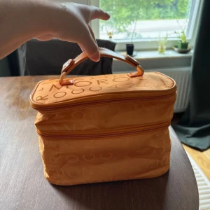 Orange necessär från Moroccanoil - Snygg och rymlig necessär i orange från Moroccanoil. Väskan har ett praktiskt handtag upptill, dubbla dragkedjor och är tillverkad i lätt polyester med Moroccanoil-logga i mönstret. Perfekt för att organisera smink eller hudvård på resan. Aldrig använd! 