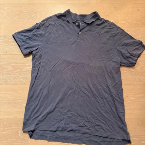 Mörkblå pikétröja från Gap XXL - Snygg mörkblå pikétröja från Gap i storlek XXL. Tröjan har klassisk krage, två knappar framtill och korta ärmar. Tillverkad i mjuk bomull som är skön mot huden. Perfekt för dig som gillar enkel och stilren design.