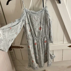 Grönblå blommig klänning från H&M - Supersöt grönblå klänning från Divided (H&M)med tunna axelband och offshoulder-långärmar. Klänningen har blommigt mönster och spetsdetaljer vid halsringningen och nederkant.