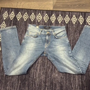 Blå jeans från J.Lindeberg - Snygga blå jeans från J.Lindeberg med klassisk femficksdesign och ljusa slitningar framtill. Jeansen har raka ben, normal passform och är tillverkade i bomullsdenim med gul kontrastsöm. Perfekta för en avslappnad och trendig look.                W = 30 L =32