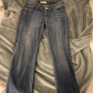 Lågmidjade blå jeans från Denim - Säljer ett par blå jeans från Denim med låg midja. Jeansen är bootcut och har snygga slitningar framtill för en avslappnad look. Perfekta för dig som gillar en enkel och tidlös stil. Materialet är mjukt och följsamt jeans.