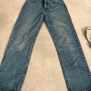 Levi's 501 blå jeans straight fit - Klassiska blå Levi's 501 jeans med rak passform och ikonisk läderpatch bak. Jeansen har fem fickor, knappgylf och är tillverkade i slitstarkt denim. Perfekta för dig som gillar en tidlös och avslappnad stil.