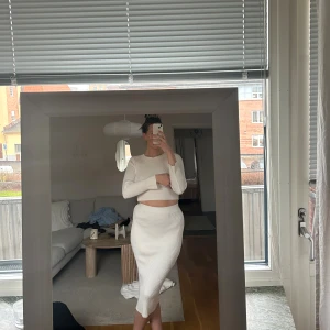 Vitt ribbat set från Nova of Sweden - Säljer ett vitt ribbad set från Nova of Sweden. Långärmad croppad överdel och en figurnära kjol med hög midja. Materialet är stickat och mjukt, perfekt för dig som gillar minimalistisk stil och vill ha något som känns både chill och trendigt. En söm i kjolens midja har dock lossnat, se bild. Lite kort i ärmarna. Setet har storlek onesize men passar mig som är en M/L.