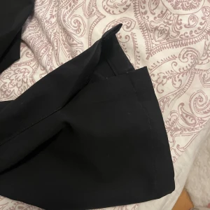 Svarta kostymbyxor med bootcut, lågmidjade  - Svarta kostymbyxor från Gina Tricot med klassisk passform och bootcut-ben. Byxorna har hällor för bälte och diskreta sidfickor. Perfekta för en stilren look och tillverkade i ett mjukt, följsamt material.