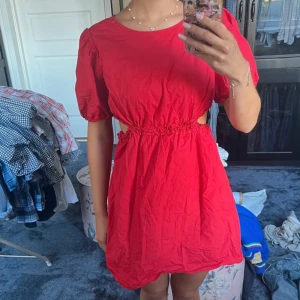 Röd kortklänning med cut-outs - Snygg röd kortklänning med puffärmar och coola cut-outs i midjan. Klänningen har rund hals och ett rynkat parti vid midjan som ger en trendig siluett. 