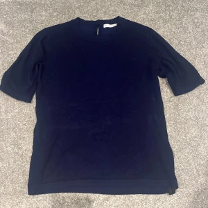 Mörkblå stickad topp från Zara - Snygg mörkblå stickad topp från Zara med rund hals och korta ärmar. Toppen har en enkel, clean look och en liten öppning med knapp i nacken. Perfekt för dig som gillar stilrena plagg med mjuk känsla.