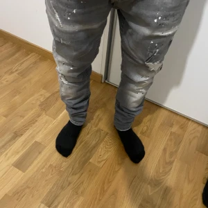 Grå jeans med slitningar och färgstänk - Säljer ett par grå jeans från Sixth June med coola slitningar och vita färgstänk. Byxorna har en slim passform och klassisk femficksdesign. Materialet är jeans och de har en modern streetstil som sticker ut.