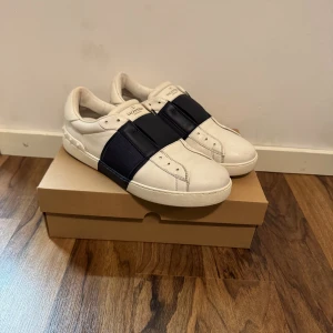 Valentino Open  vit/marinblå - Snygga Valentino Open sneakers i vitt skinn med bred marinblå rem över vristen. Skorna är i storlek 42 men passar lite även lite större. Bra skick, inga större defekter. Inget fast.