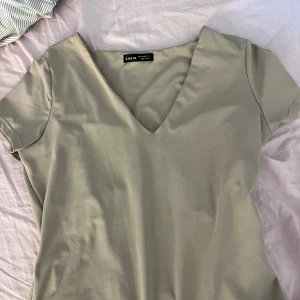 Beige v-ringad body från SHEIN - En stilren beige body från SHEIN med v-ringning och korta ärmar. Bodyn har en enkel och clean design som gör den lätt att matcha med olika accessoarer. 