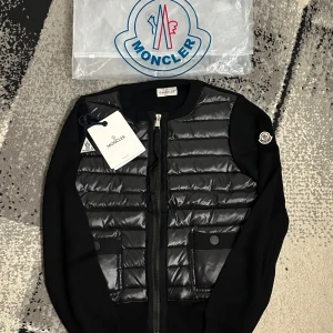Moncler cardigan  - Snygg svart dunväst från Moncler med quiltad framsida och två fickor med knappdetalj. Västen har dragkedja framtill och Moncler-logga på ärmen. Perfekt för lager-på-lager och ger en sportig vibe.