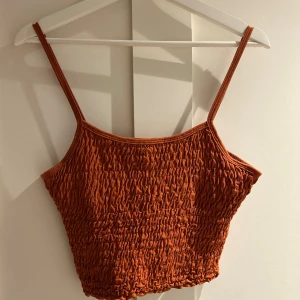 Rostfärgad croppad linnetopp Gina Tricot - Säljer en snygg croppad linnetopp från Gina Tricot i rostbrun färg. Toppen har smala axelband och är tillverkad i ett mjukt, rynkat bomullsmaterial som ger en cool textur. Perfekt för dig som gillar trendiga och bekväma plagg med lite edge.