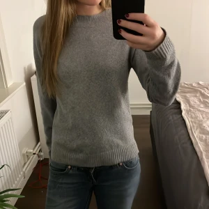 Grå stickad tröja  - Mysig grå stickad tröja från Vero Moda i storlek XS. Tröjan har rund hals, ribbade muddar och långärmad passform. Perfekt för dig som gillar enkel och clean stil. Materialet är mjukt och känns skönt mot huden. Tröjan är lite nopprig
