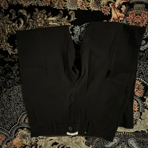 Svarta cargo shorts från Only & Sons - Svarta cargo shorts från Only & Sons med raka ben och stora sidofickor. Snygg minimalistisk look med knappstängning och bälteshällor. Perfekta för chill dagar och streetwear. Materialet känns som bomull och ger en skön känsla mot huden.