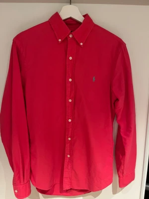 Röd skjorta från Polo Ralph Lauren - Snygg röd skjorta från Polo Ralph Lauren i slim fit. Klassisk button-down krage, vita knappar och broderad logga på bröstet. Tillverkad i mjuk bomull, perfekt för dig som gillar stilrena och färgstarka plagg. Pris kan diskuteras 