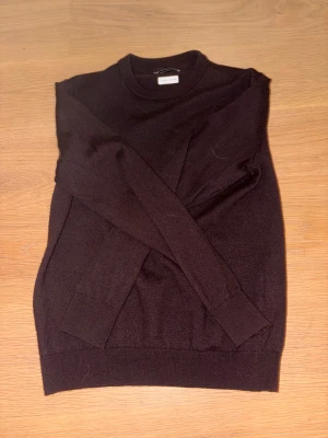 Vinröd merinotröja These Glory Days - Superskön mörkbrun tröja från These Glory Days i Superior Merino-ull. Klassisk rund hals och långärmad modell med ribbade muddar vid ärmslut och nederkant. Perfekt för dig som gillar stilrena och mjuka plagg med premiumkänsla.