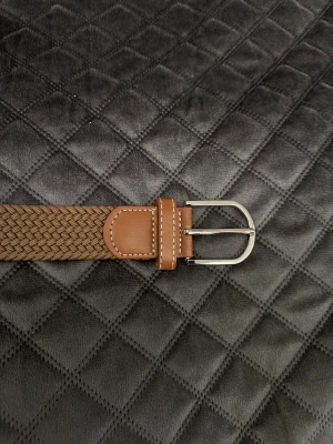 Brunt flätat bälte med skinn-detaljer - Snyggt brunt flätat bälte med detaljer i ljusbrunt skinn och silvrigt spänne. Bältet har en stilren look med vit söm på skinnet och är flexibelt tack vare den vävda strukturen. Perfekt för att ge outfiten en chill och modern touch.
