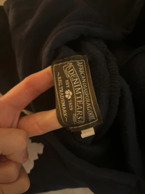 Mörkblå hoodie från Denim Tears - Säljer en mörkblå hoodie från Denim Tears med vita blommönster över hela tröjan. Hoodien har huva och långa ärmar, perfekt för dig som gillar streetwear och vill sticka ut med en unik design. Materialet känns mjukt och skönt mot huden.