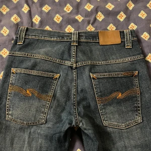 Blå Nudie Jeans W29 L32 - Snygga blå jeans från Nudie Jeans med klassisk orange söm och vågig brodyr på bakfickorna. Modellen har fem fickor, knapp och dragkedja framtill samt normal passform. Perfekt för dig som gillar stilrena jeans. Skick 10/10 använd endast fåtal gånger, storlek w29 l32. Fråga gärna om det är nåt ni undrar!!