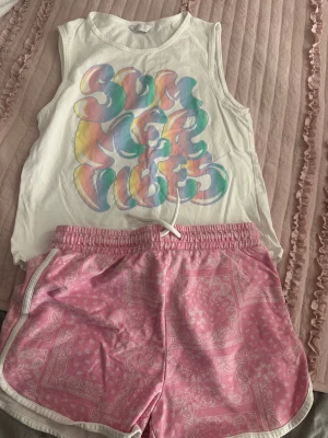 Rosa bandanamönstrade shorts med snörning - Säljer ett par rosa shorts med vitt bandanamönster och vit kant. De har elastisk midja med snörning framtill och är gjorda i ett mjukt bomullsmaterial. Perfekta för chill dagar och sommarhäng.