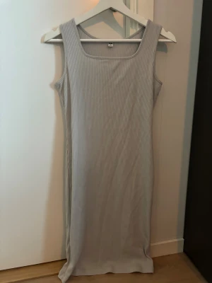 Ljusgrå ribbad ärmlös klänning - Säljer en ljusgrå ribbad klänning från H&M med fyrkantig ringning och ärmlös design. Klänningen är figurnära och har en mjuk, stretchig känsla som sitter snyggt på kroppen. Perfekt för dig som gillar enkel och stilren look.