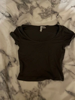 Svart croppad topp från Divided - Svart, enkel och croppad topp från Divided med rundad halsringning och korta ärmar. Tillverkad i mjuk bomull som känns skön mot huden. Perfekt att styla med jeans eller kjol för en chill look.