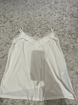Vit linnetopp med spets från Amisu - Säljer en vit linnetopp från Amisu i storlek S. Toppen har tunna axelband och v-ringad hals med dekorativ spets upptill. Materialet är mjukt och lent, perfekt för en fräsch och clean look. Spetsen ger en extra touch av stil och feminin vibe.