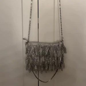 Silvrig väska med diamant detaljer  - Silvrig väska med små diamant detaljer. Väskan har inga täcken på användning och är som ny. Bredd: 5 cm. Djup: 17 cm. Längd: 22 cm.💗