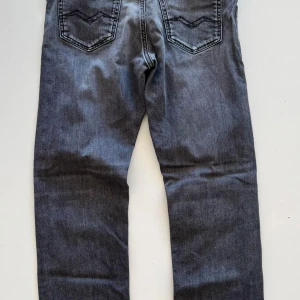 Mörkgrå raka jeans från Replay - Snygga mörkgrå jeans från Replay med klassisk femficksdesign och raka ben. Jeansen har diskreta slitningar och tydliga sömmar på bakfickorna. Perfekta för en avslappnad och stilren look. sen så ser man att replay tyget på baksidan är av sänker därav priset men märks inye under en tröja eller tshirt.