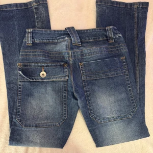Blå jeans med stora bakfickor - Snygga blå jeans med markerad tvätt och kontrastsömmar. Byxorna har stora bakfickor, varav en med lock och knapp, samt klassiska bälteshällor. Jeansen har rak passform och är tillverkade i denim med en cool vintagekänsla. Märkta xl men mycket mindre i storlek