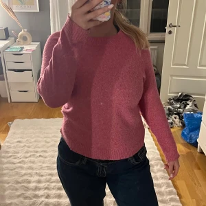 Rosa stickad tröja från Vero Moda - Mysig rosa stickad tröja från Vero Moda i storlek M. Tröjan har rund halsringning, långa ärmar och ribbade muddar vid ärmslut och nederkant. Perfekt för kyliga dagar och enkel att matcha med jeans eller kjol.