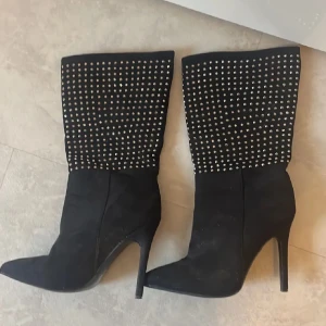Svarta boots med nitar och hög klack -  Skorna har spetsig tå och hög klack. Tillverkade i syntetmaterial med mockakänsla. Bara haft på mig en gång