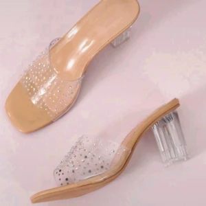 Beige sandaler med transparent klack - Snygga sandaler i beige med transparent rem över foten dekorerad med små glittriga stenar. Skorna har fyrkantig tå och en genomskinlig klack som ger en modern vibe. Perfekta för att lyfta din outfit med en touch av glamour.