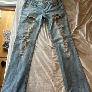 Ljusblå slitna jeans - Ljusblå jeans från Monki med rejält slitna och trasiga detaljer längs båda benen. Klassisk femficksmodell med raka ben och låg midja. Jeansen har en cool, avslappnad vibe och är tillverkade i bomullsdenim.mått 40 midja innerbenslängd 82